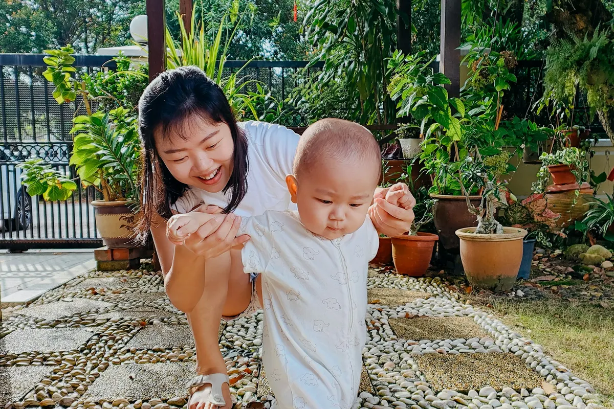 Maman souriante aidant son bébé à faire ses premiers pas au jardin